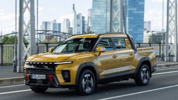 Ein goldfarbener KGM Musso EV fährt über eine Main-Brücke in Frankfurt
