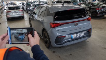 Cupra Born steht in einer Halle zur Leasingrückgabe und wird von einem TÜV-Mitarbeiter von hinten fotografiert