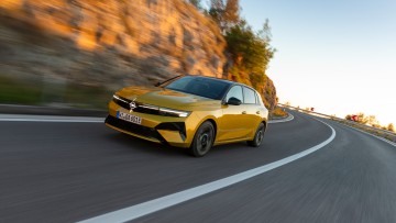 Gelber Opel Astra fahrend vor Steinwand von vorn fotografiert