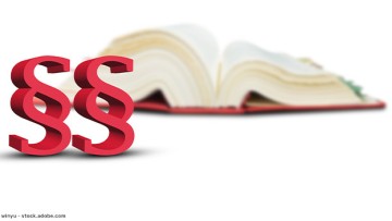 Paragraphen-Symbole im Vordergrund, im Hintergrund ein aufgeschlagenes Gesetzbuch.