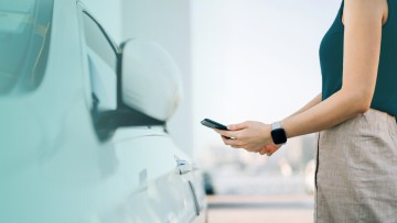 Frau steht mit Smartphone vor ihrem Auto
