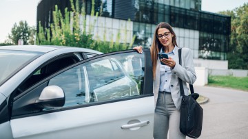 Businessfrau steigt ins Auto ein und sieht dabei auf ihr Smartphone