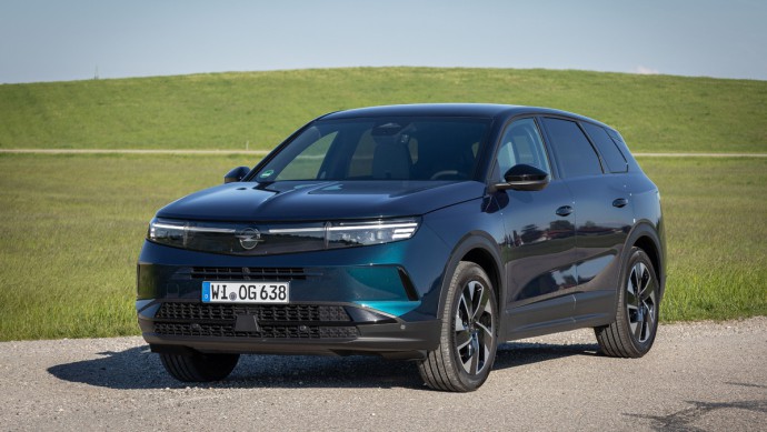 Opel Grandland Hybrid Opel Grandland Hybrid stehend vor grüner Wiese mit leichtem Hügel im Hintergrund