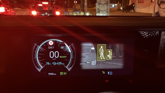 Ansicht des Kombiinstruments mit eingeblendeter Nachtsicht-Funktion, die zwei Personen an der Bushaltestelle sichtbar macht.