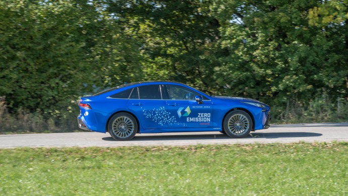 Blau lackierter Toyota Mirai fahrend vor Wald