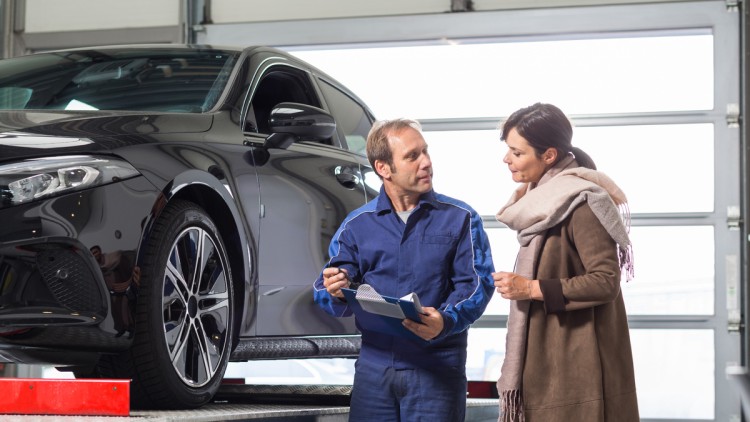 Auto auf Hebebühne mit Kundendienstmeister und Kundin im Gespräch am Auto