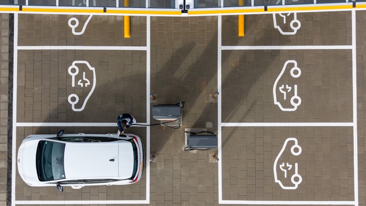 Sachsen, Klipphausen: Ein Mann steht in einem Ladepark der EnBW Energie Baden-Württemberg AG und steckt ein Ladekabel in den Tankstutzen eines Elektroautos (Aufnahme mit einer Drohne).