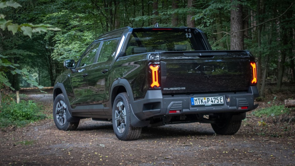 Von hinten fotografierter KGM Musso EV in schwarz auf einem Waldweg