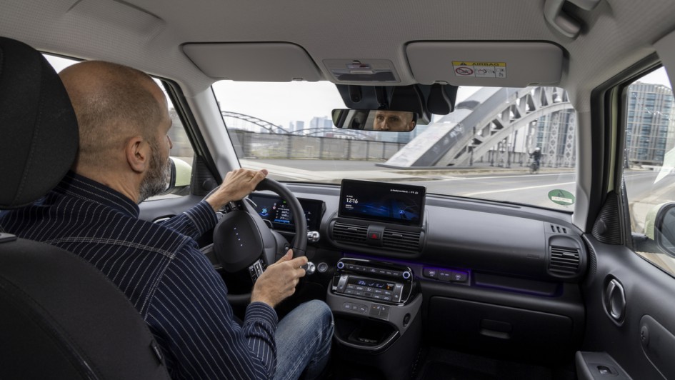 Aufnahme von der Rückbank über die Schulter des Fahrers im Hyundai Inster während der Fahrt über eine Brücke in Frankfurt