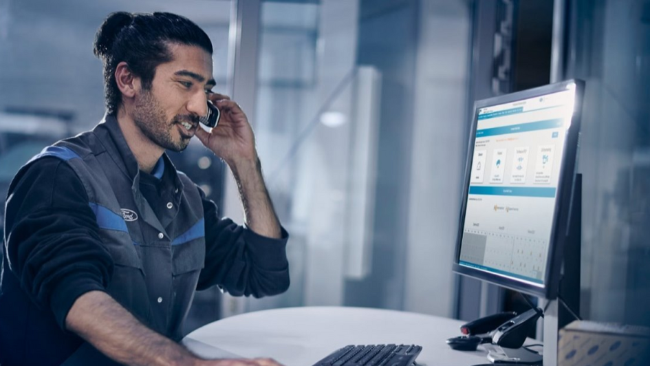 Werkstattmeister hat Telefon am Ohr und schaut in Monitor bei der Terminvergabe