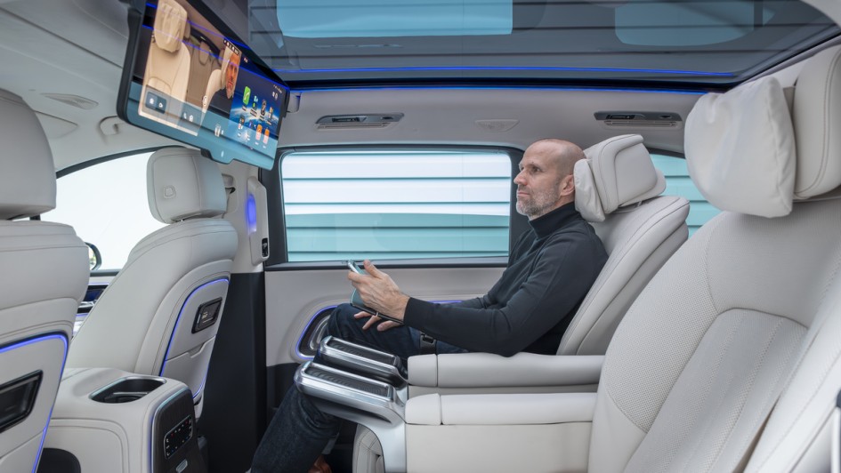 Mittlere Sitzreihe im Mercedes VLE mit Mann der auf den riesigen Bildschirm schaut, der oben am Dach befestigt ist.